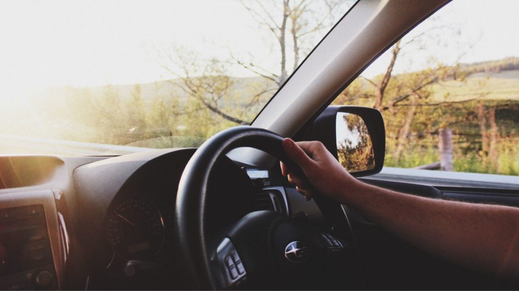 Hand on a steering wheel with trees outside the vehicle.